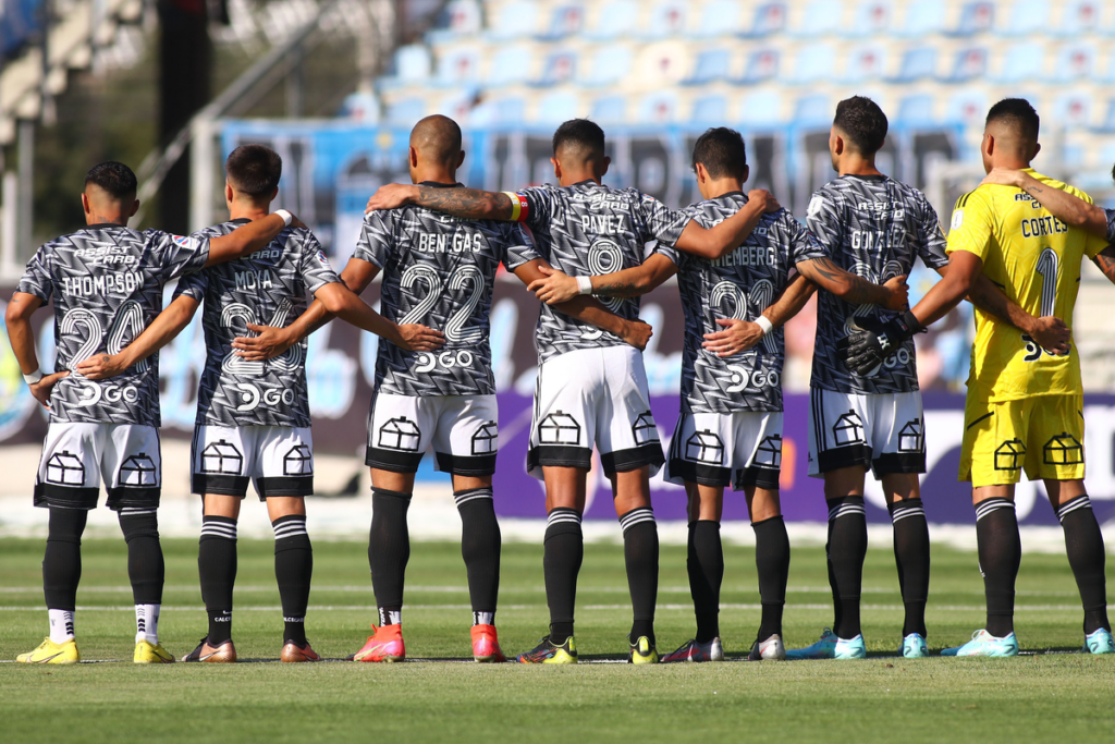 Jugadores de Colo-Colo se abrazan en el centro del terreno de juego en medio de un minuto de silencio en la derrota 5-1 sufrida a manos de O'Higgins, válido por la segunda fecha del Campeonato Nacional 2023.