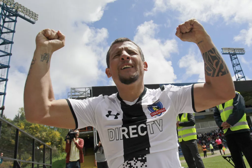 Emiliano Vecchio celebrando un gol con los brazos en alto con la camiseta de Colo-Colo.