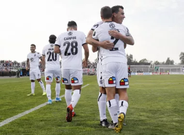 Esteban Paredes abraza a Gabriel Costa tras anotar un gol con la camiseta de Colo-Colo durante la temporada 2019 en el Estadio Municipal de La Cisterna, mientras que el resto de sus compañeros camina al círculo central.