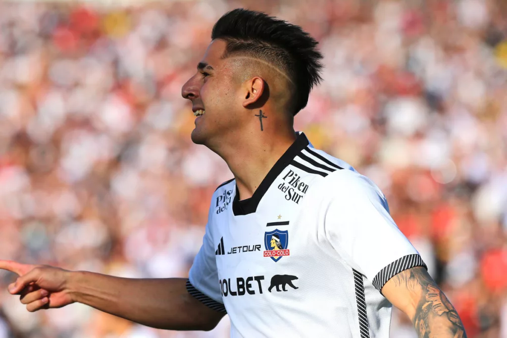 Guillermo Paiva de perfil celebra un gol con la camiseta de Colo-Colo con una notoria sonrisa en su rostro.