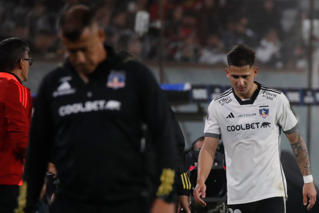 Guillermo Paiva se retira del campo de juego con claros signos de dolor, mientras que al frente suyo se encuentra Jorge Almirón, entrenador de Colo-Colo con la cabeza cabizbaja.