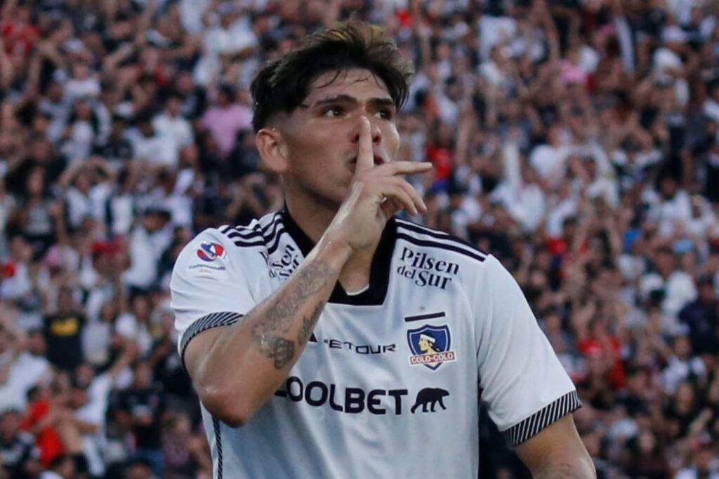 Carlos Palacios celebrando un gol mientras hace silencio con su mano.