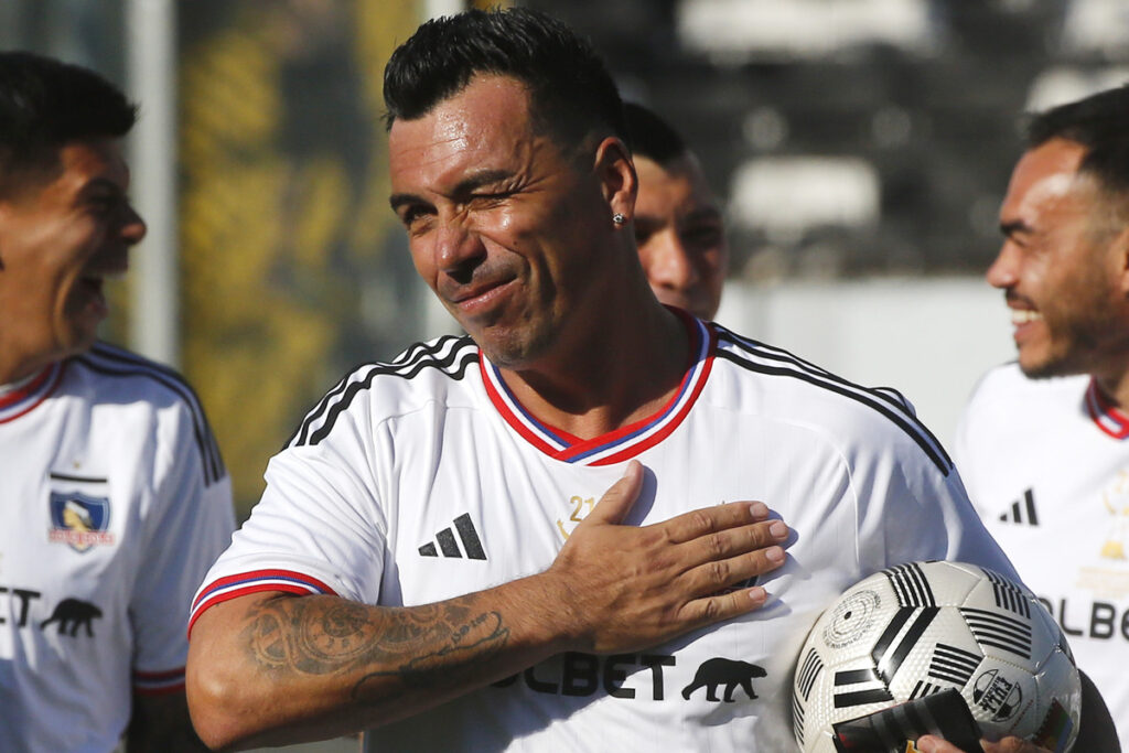 Primer plano de Esteban Paredes guiñando un ojo y una mano en el escudo de Colo-Colo.