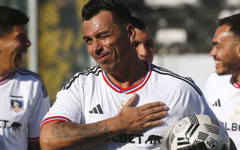 Primer plano de Esteban Paredes guiñando un ojo y una mano en el escudo de Colo-Colo.