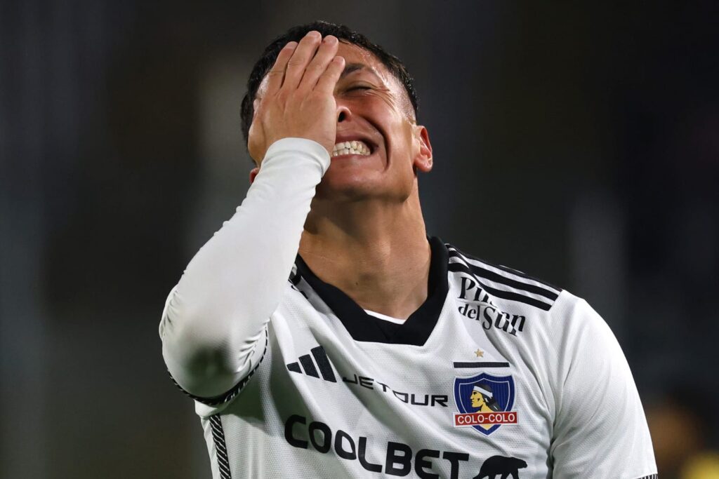 Primer plano a Cristián Zavala tapándose la cara con indumentaria de Colo-Colo.