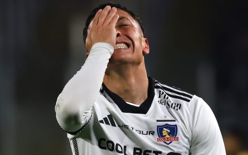 Primer plano a Cristián Zavala tapándose la cara con indumentaria de Colo-Colo.