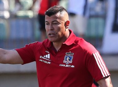 Jorge Almirón con camiseta roja de Colo-Colo en el banco de suplentes.