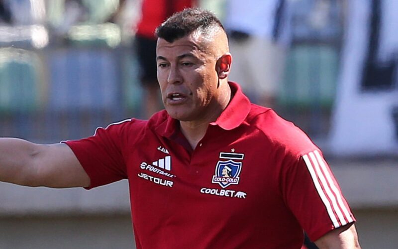 Jorge Almirón con camiseta roja de Colo-Colo en el banco de suplentes.